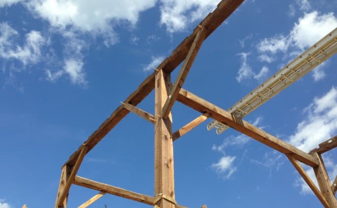 Looking up towards a timber frame rising into the blue sky.