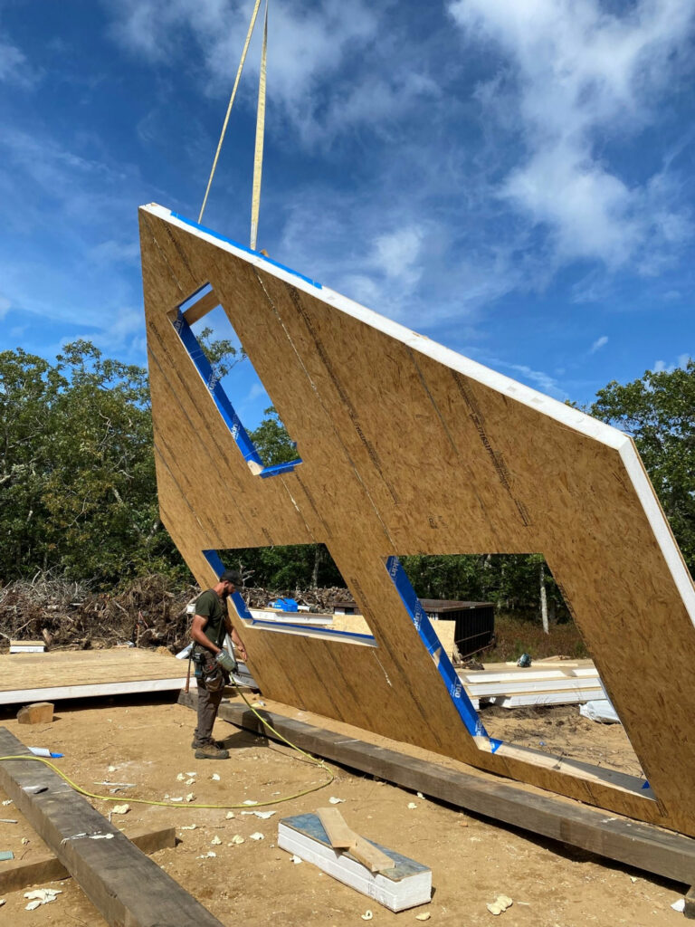 A large panel end of a timber frame home is hoisted by crane.