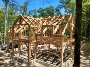 A timber frame structure under construction sits in a forest
